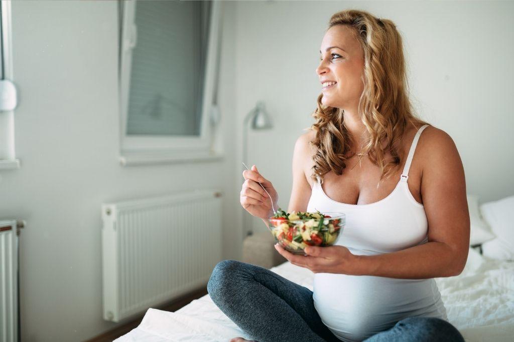Raskaana oleva nainen syö salaattia.
