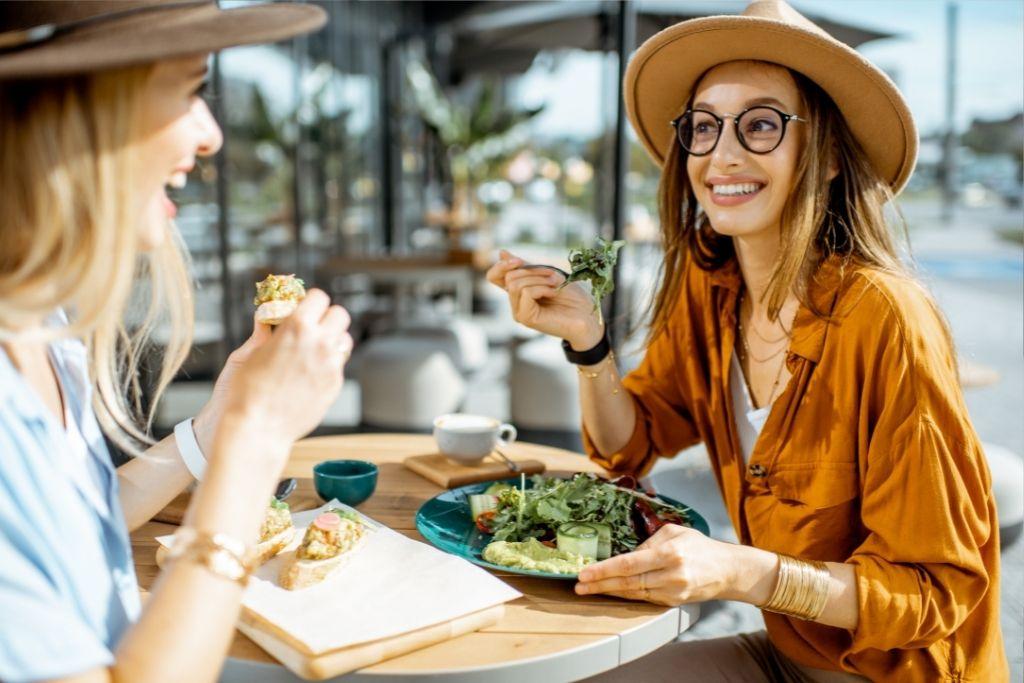 Nuoret naiset syövät terveellistä ruokaa saman pöydän ääressä.