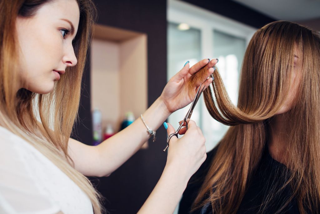 Kampaaja tasoittaa naisen pitkiä hiuksia.