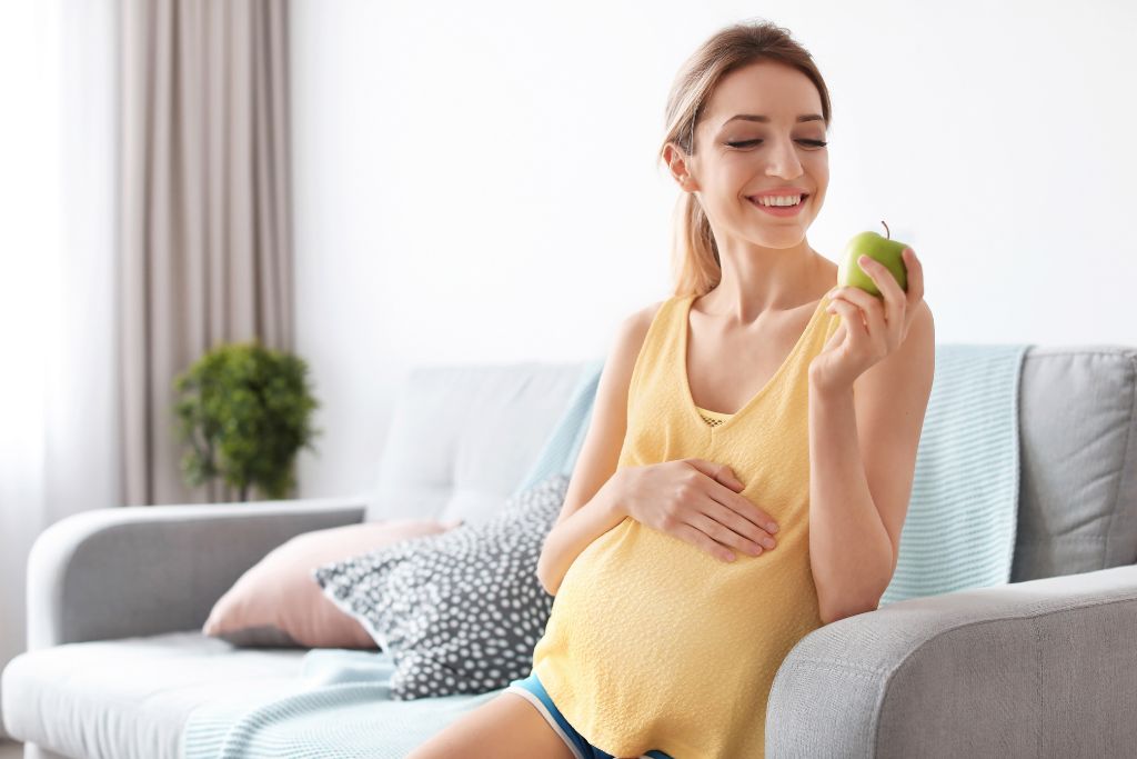 Raskaana oleva nainen syö omenaa estääkseen raskauspahoinvointia.